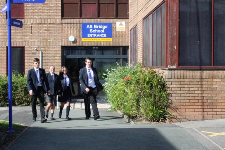 A photograph of three school students outside the main entrance to Alt Bridge School